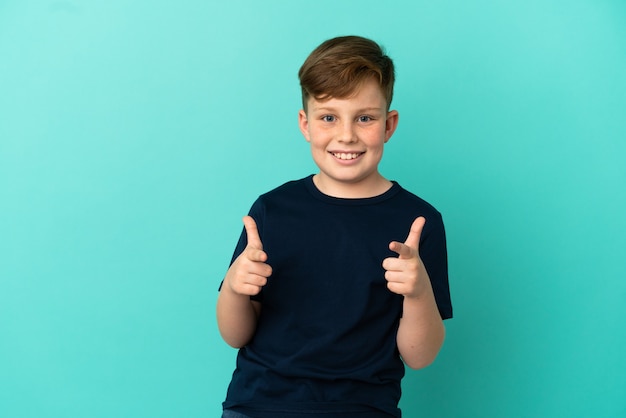 Foto garotinho ruivo isolado em um fundo azul apontando para a frente e sorrindo