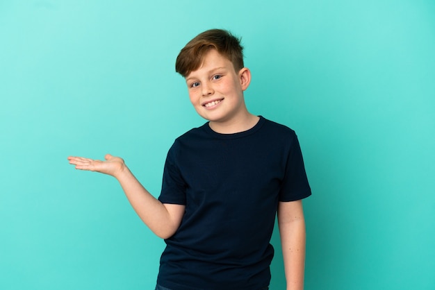 Foto garotinho ruivo isolado em um fundo azul apresentando uma ideia enquanto olha sorrindo para