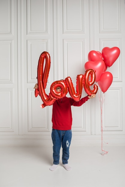 Garotinho se cobriu com um balão vermelho de amor em um fundo branco