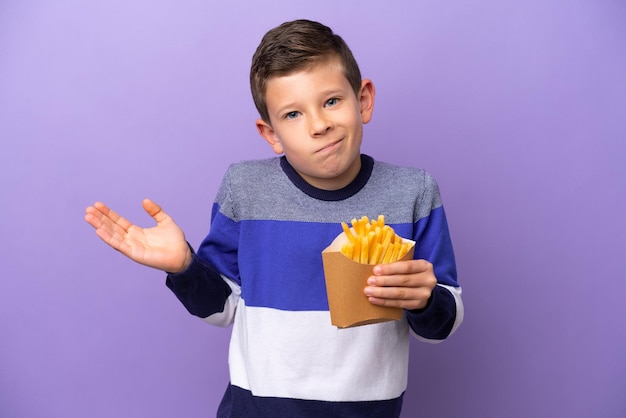 Garotinho segurando batatas fritas isoladas em fundo roxo com dúvidas ao levantar as mãos