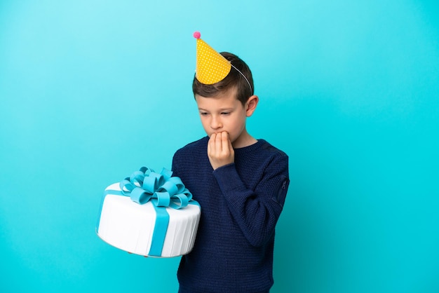 Garotinho segurando bolo de aniversário isolado em fundo azul com dúvidas