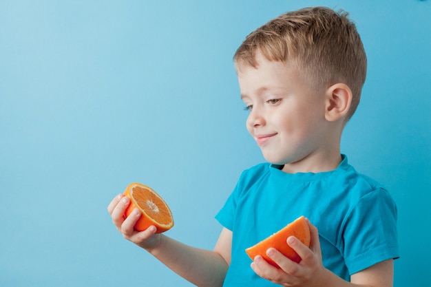 Foto garotinho segurando uma laranja nas mãos sobre fundo azul, dieta e exercício para o conceito de boa saúde