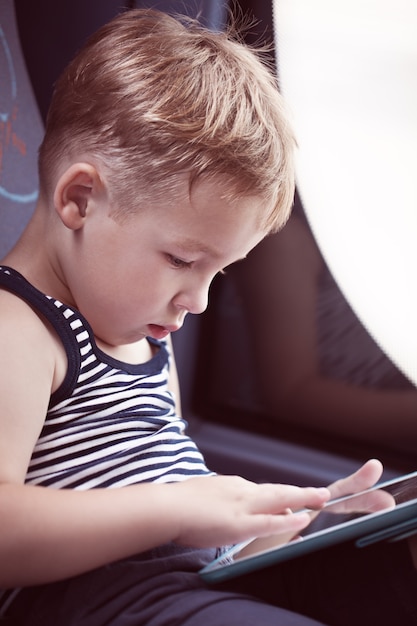 Garotinho sentado à janela no ônibus e usando o touch pad para entreter-se