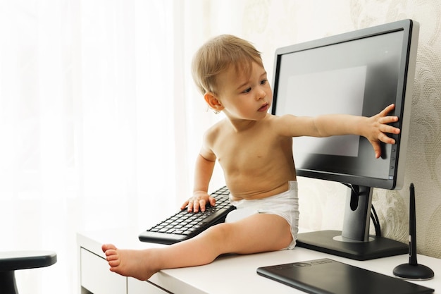 Garotinho sentado em uma mesa e brincando com um teclado e monitor