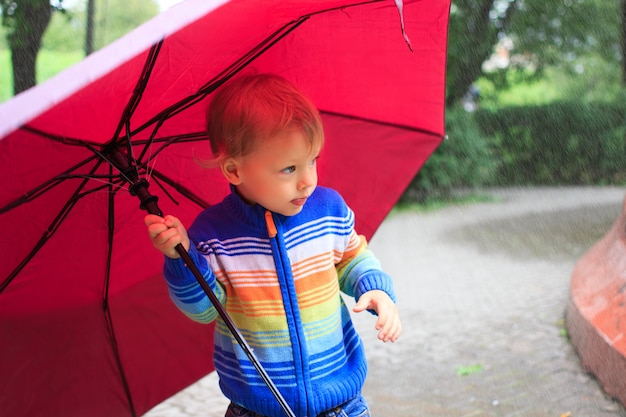 Garotinho sob o guarda-chuva, olhando a chuva