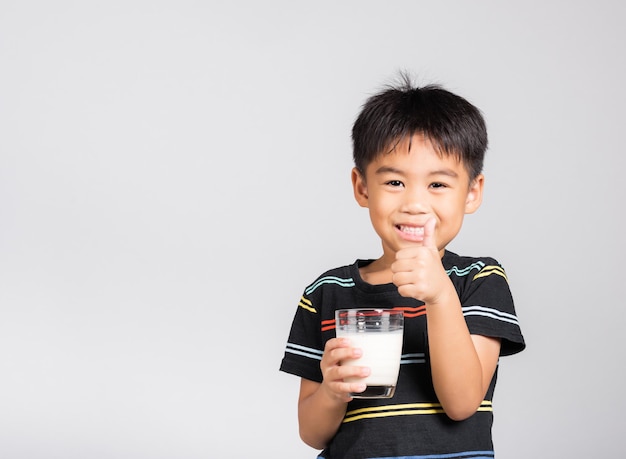 Garotinho sorria segurando o copo de leite, ele bebendo leite branco e mostra o polegar no dedo