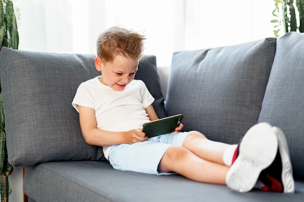 Garotinho usando smartphone enquanto estava deitado no sofá em casa