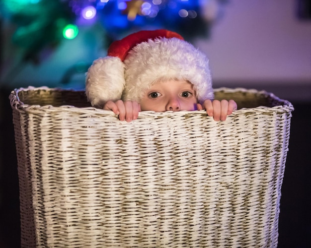 Garotinho vestido de Papai Noel sentado em uma grande cesta