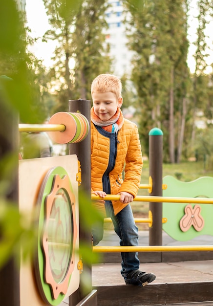 Garoto adolescente alegre ruivo em roupas amarelas sorrindo brincando no playground moderno no parque da cidade