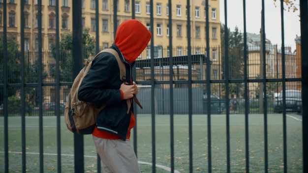Garoto adolescente com costas andando perto do campo de futebol da escola