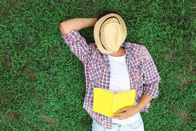 Garoto adolescente com livro deitado na grama verde