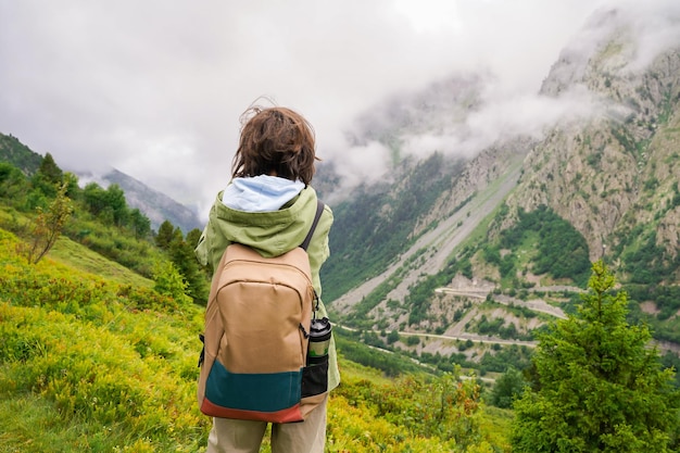 Garoto adolescente com mochila nas montanhas admirando a paisagem cênica menino caminhando e caminhando atividades de verão para crianças