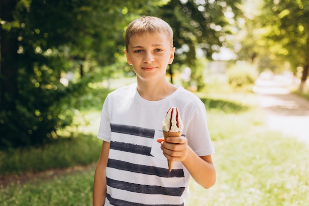 Garoto adolescente comendo casquinha de sorvete no fundo verde da natureza. Verão, junk food e conceito de pessoas