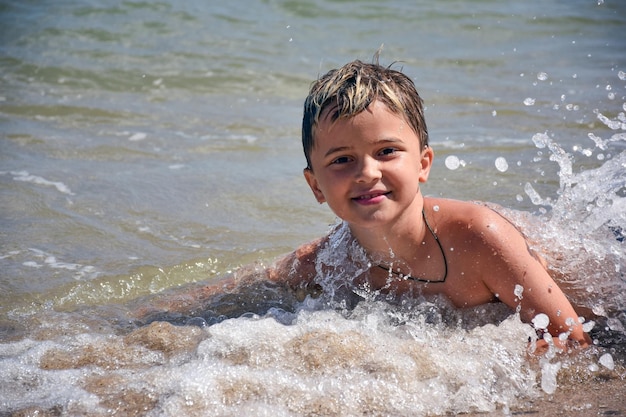 Garoto adolescente de raça branca se banha no mar em ondas e spray e sorrisos