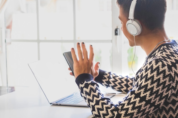 Garoto adolescente em videochamada com celular enquanto usa o laptop usando fones de ouvido Garoto do milênio desfrutando de tecnologia e aplicativo social