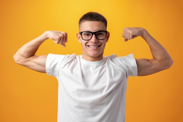 Garoto adolescente muscular caucasiano mostra sua força contra o fundo amarelo