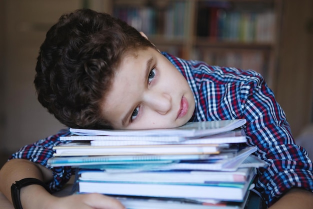 Garoto adolescente se senta em uma mesa e dorme em uma pilha de livros Treinando em casa na quarentena de coronavírus Foco seletivo Fundo desfocado