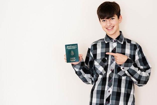 Garoto adolescente segurando o passaporte da Tunísia parecendo positivo e feliz em pé e sorrindo com um sorriso confiante contra o fundo branco