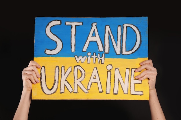 Garoto adolescente segurando pôster Stand com a Ucrânia contra fundo preto closeup