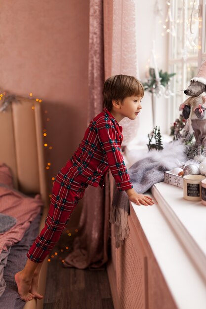 Garoto adorável, olhando pela janela, esperando o Papai Noel