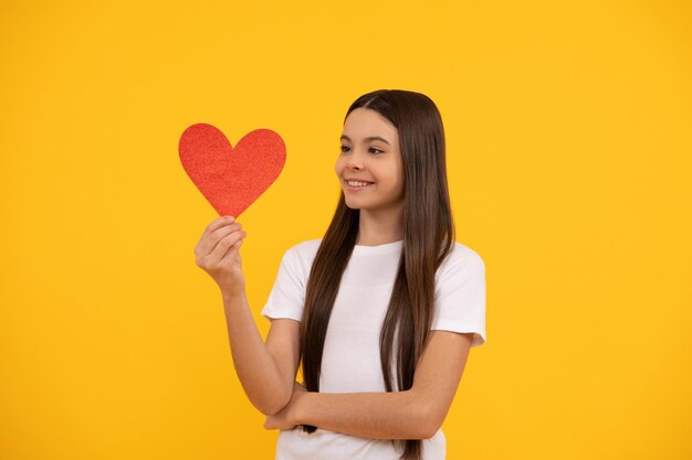 Garoto alegre com presente romântico de amor. amada. venda dos namorados. retrato de criança com coração. feliz Dia dos namorados. seja meu namorado. menina adolescente em fundo amarelo. amor presente.