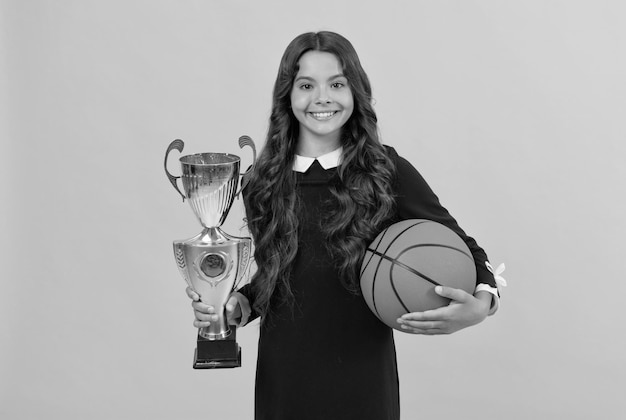 Garoto alegre segura bola de basquete e taça de campeão no sucesso esportivo de fundo amarelo