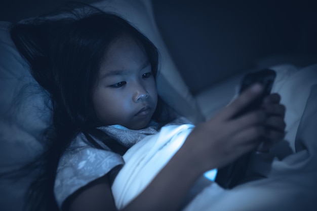 Garoto asiático jogando no smartphone na cama à noitea garota viciada nas mídias sociais