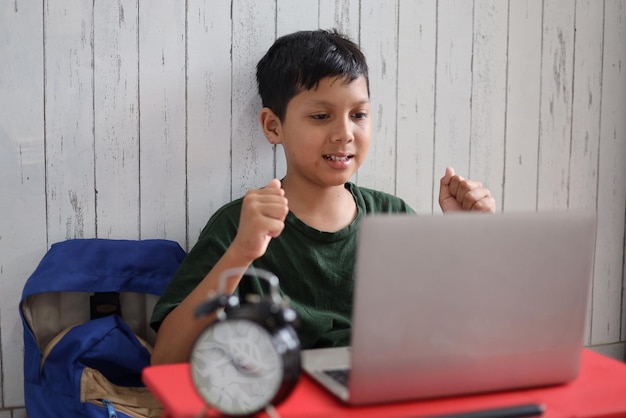 Garoto asiático mostrando expressão animada olhando para o laptop e gesticulando sim apertando o punho cerrado