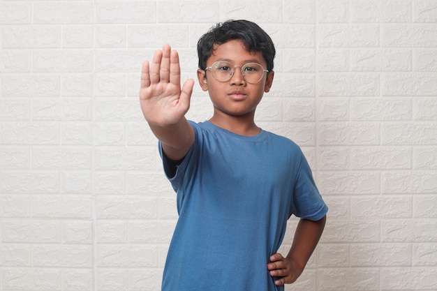Garoto asiático usando óculos com a mão aberta fazendo o sinal de stop e expressão séria