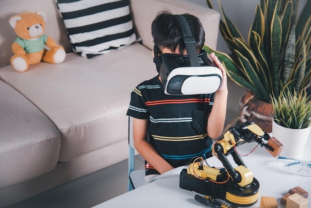 Garoto asiático usando óculos VR no braço robótico na oficina