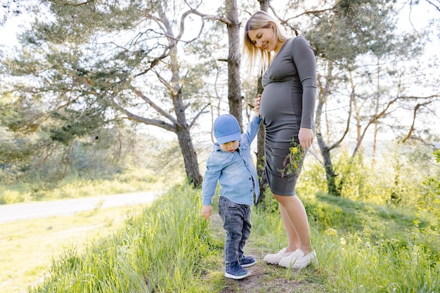 Garoto bonito acariciando a barriga grávida da mãe na floresta Mãe grávida e seu filho caminhando e passando um tempo divertido juntos