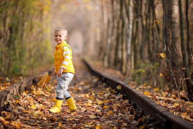 Foto garoto bonito andando em uma ferrovia sorrindo túnel de amor no outono no lugar romântico do outono