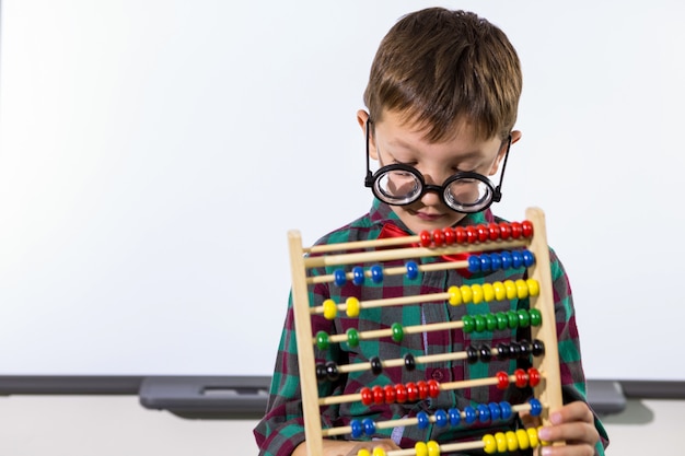 Garoto bonito brincando com ábaco na sala de aula