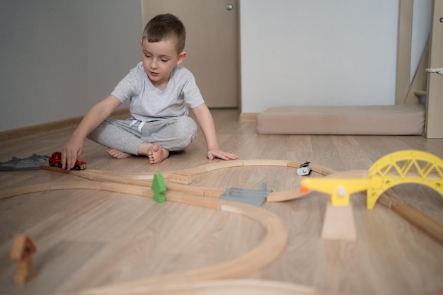 Garoto bonito brincando com ferrovia de madeira em casa