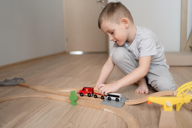 Garoto bonito brincando com ferrovia de madeira em casa