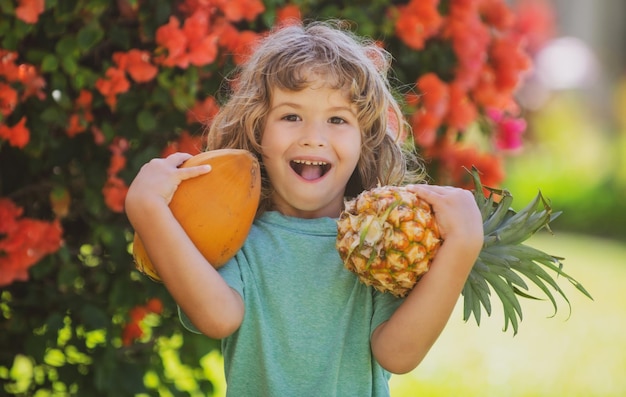 Garoto bonito com abacaxi e coco no jardim tropical frutas tropicais frescas para a vida saudável das crianças