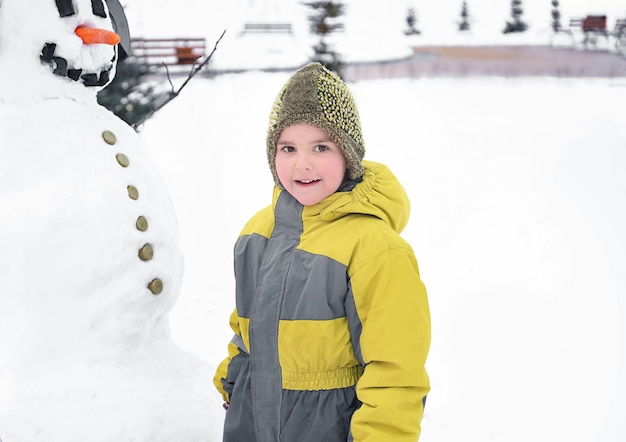 Garoto bonito com boneco de neve no parque nas férias de inverno