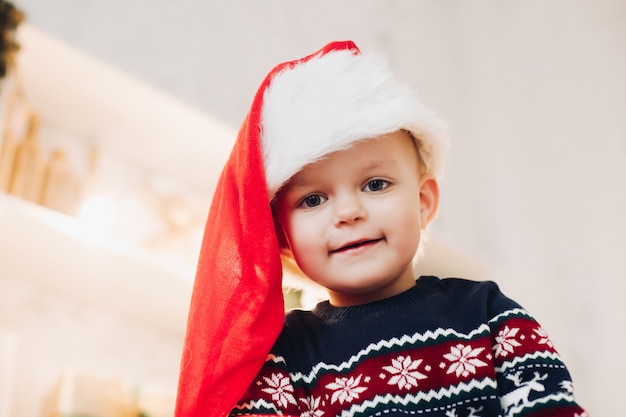 Garoto bonito com chapéu de Papai Noel e camisola de inverno.