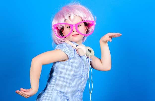 Garoto bonito com fones de ouvido fundo azul Fones de ouvido de menina pequena dançando peruca rosa Criança usando tecnologia para se divertir Fones de ouvido modernos Dança de movimento de energia Inspirado pela música Criança ouvindo música