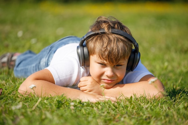 Garoto bonito com fones de ouvido, ouvindo música, deitado na grama