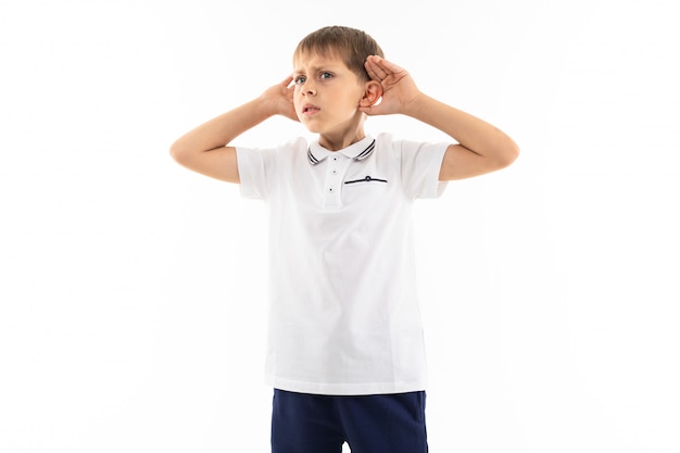 Garoto bonito com franja em uma camiseta branca ouve os sons em um fundo branco com espaço de cópia