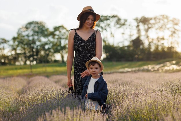 Garoto bonito de chapéu caminha de mãos dadas com sua mãe por um campo de lavanda