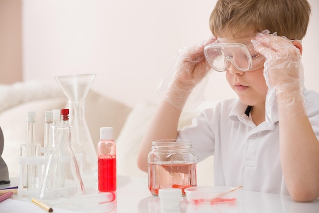 Garoto bonito de óculos fazendo experimentos científicos Criança trabalhando com líquidos
