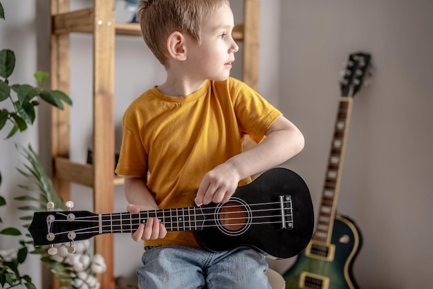 Garoto bonito e alegre está tocando violão ukulele na sala de música Alegre aprendendo a tocar instrumentos musicais