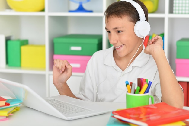 Garoto bonito em fones de ouvido usando laptop em casa