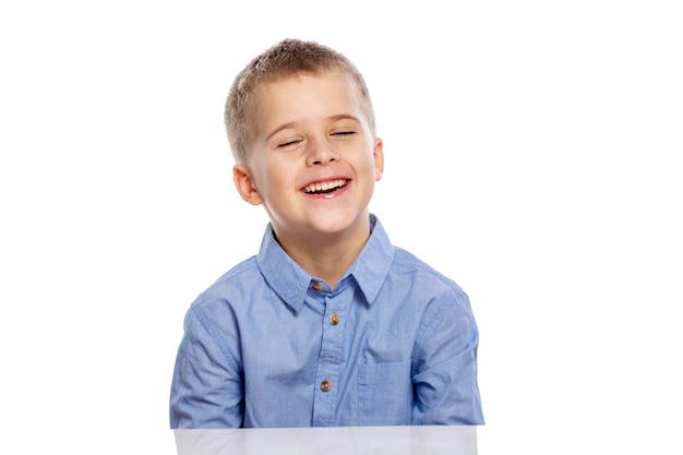 Garoto bonito em idade escolar se senta à mesa e ri. Isolado em um fundo branco.