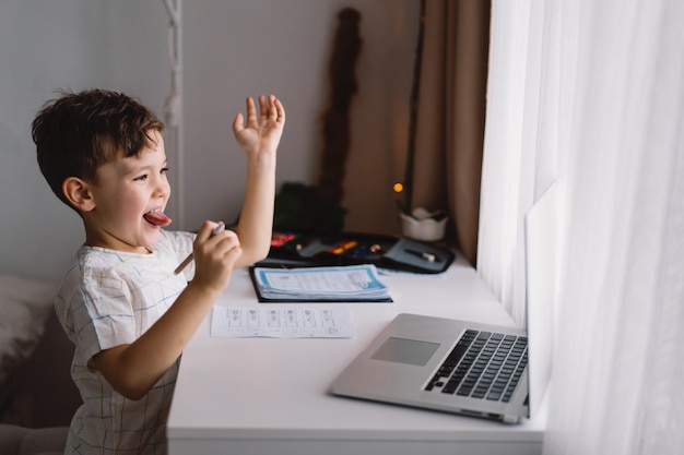 Garoto bonito estudando em casa com laptop e fazendo lição de casa da escola