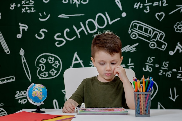 Garoto bonito fazendo lição de casa Garoto inteligente desenhando na mesa Aluno da escola primária desenhando no local de trabalho Garoto gosta de aprender Educação em casa De volta à escola Garotinho na lição da escola