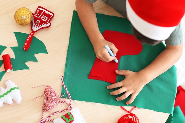 Garoto bonito fazendo meia de feltro de natal na mesa