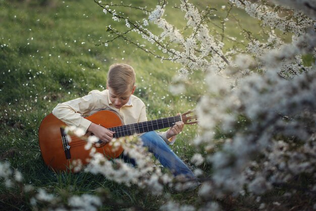 Garoto bonito fazendo música tocando guitarra na natureza.